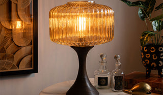 The Amber Glass & Wooden Base Table Lamp styled on a table with various accessories and a plant.