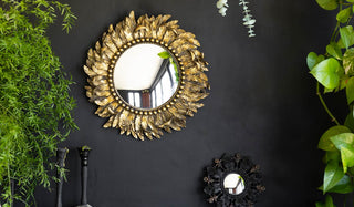 The Golden Feather Round Wall Mirror and Small Black Flowers & Leaves Convex Mirror displayed on a black wall, styled with plants and candlesticks.
