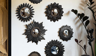 Various black decorative mirrors styled on a white wall next to a framed artwork and a plant.