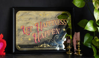 The Let Happiness Happen Mirror Wall Art styled on a dark surface with some candles, candlestick holders and greenery.