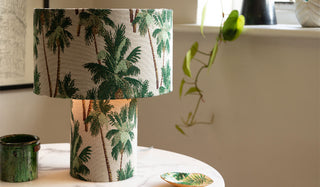 A palm print table lamp styled on a table with various accessories and a plant in the background.