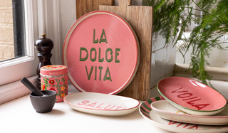 Various colourful and wooden kitchen items arranged together by a kitchen window, styled with a plant in the background.