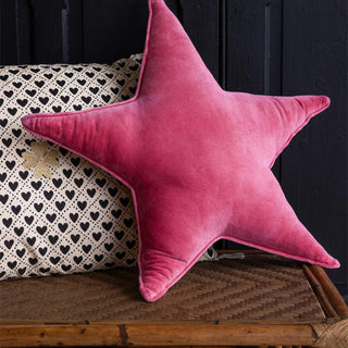 A pink cushion in the shape of a star, styled on a wicker bench with another cushion.