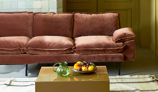 A velvet sofa styled behind a rug, coffee table, jug and fruit bowl.