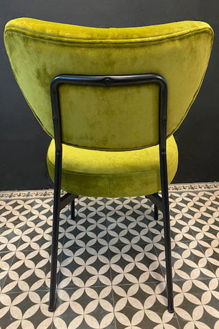 The back of the green velvet chair showing the black metal frame and chair legs.