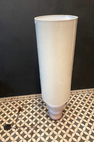 A off-white floor lamp on a tiled floor. The shade is wrapped in plastic.