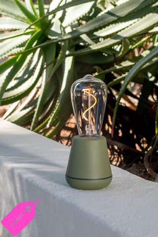 A beautiful green outlet product with a lit filament on a white outdoor wall.