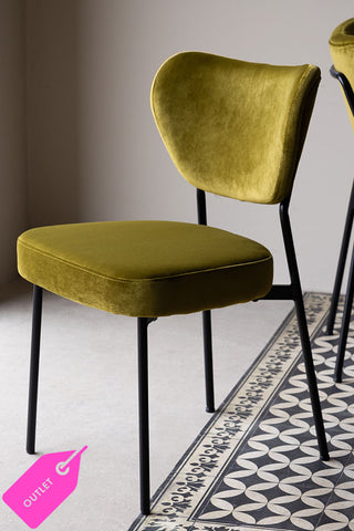 The Needlecord Velvet Green Dining Chair styled on a geometric floor with a bright pink 'outlet' sticker in the bottom left hand corner.