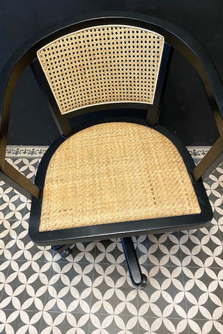 Black swivel chair with cane seat pads and a cane back in a dark setting