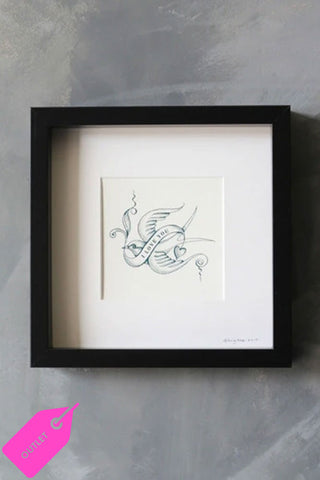 A bird tattoo art print with the words 'i love you' in a banner across the front. The handdrawn print is framed with a white border and black frame. It is hung on a grey stonewashed wall.