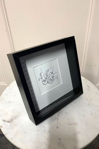 A black framed art print on a white marble side table.