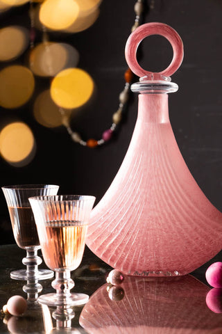 Beautiful pink glass decanter in a festive setting. Next to the decanter is two wine glasses and mini baubles in pink.