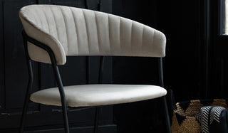 A grey velvet dining chair styled in front of a black sideboard, next to a basket with a blanket inside.