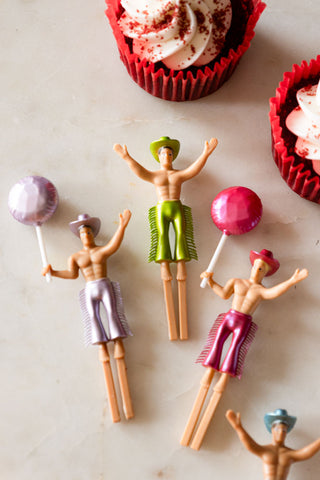 The Set of 4 Cowboy Cake Toppers displayed on a white surface with some cupcakes in red cases.