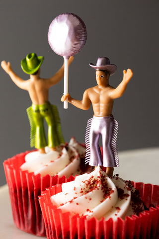 Close-up of two of the Set of 4 Cowboy Cake Toppers displayed in cupcakes in red cases.