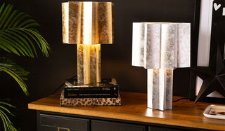 Two star lamps in gold and silver, styled on a wooden sideboard with books, an art print, ornaments and some greenery.