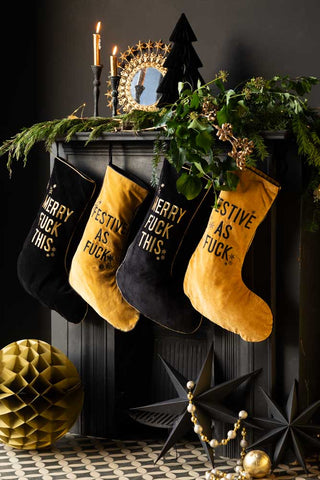 four stockings in a velvet black and gold on a fireplace which is dressed for christmas.