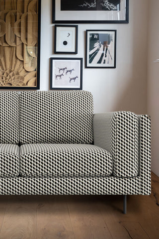 Close-up of The Grace Medium Sofa In Geo Glam Woven Sand & Black styled in a living room in front of a white wall decorated with various framed art prints.