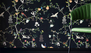 Black chinoiserie wallpaper styled on the wall behind a green velvet dining chair.