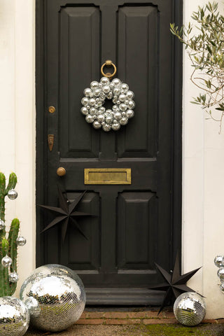 Silver disco ball wreath on a black door styled with black paper stars and disco balls.