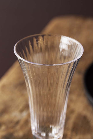 Close-up detail image of the Ribbed Glass Champagne Flute on wooden table with dark wall background