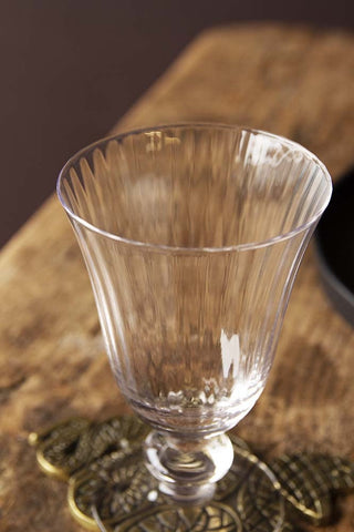 Close-up detail image of the Ribbed Glass Wine Glass on gold snake coaster on wooden surface with dark wall background